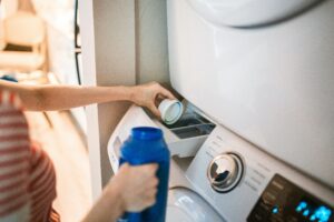echando detergente bote azul en el cajetín de la lavadora